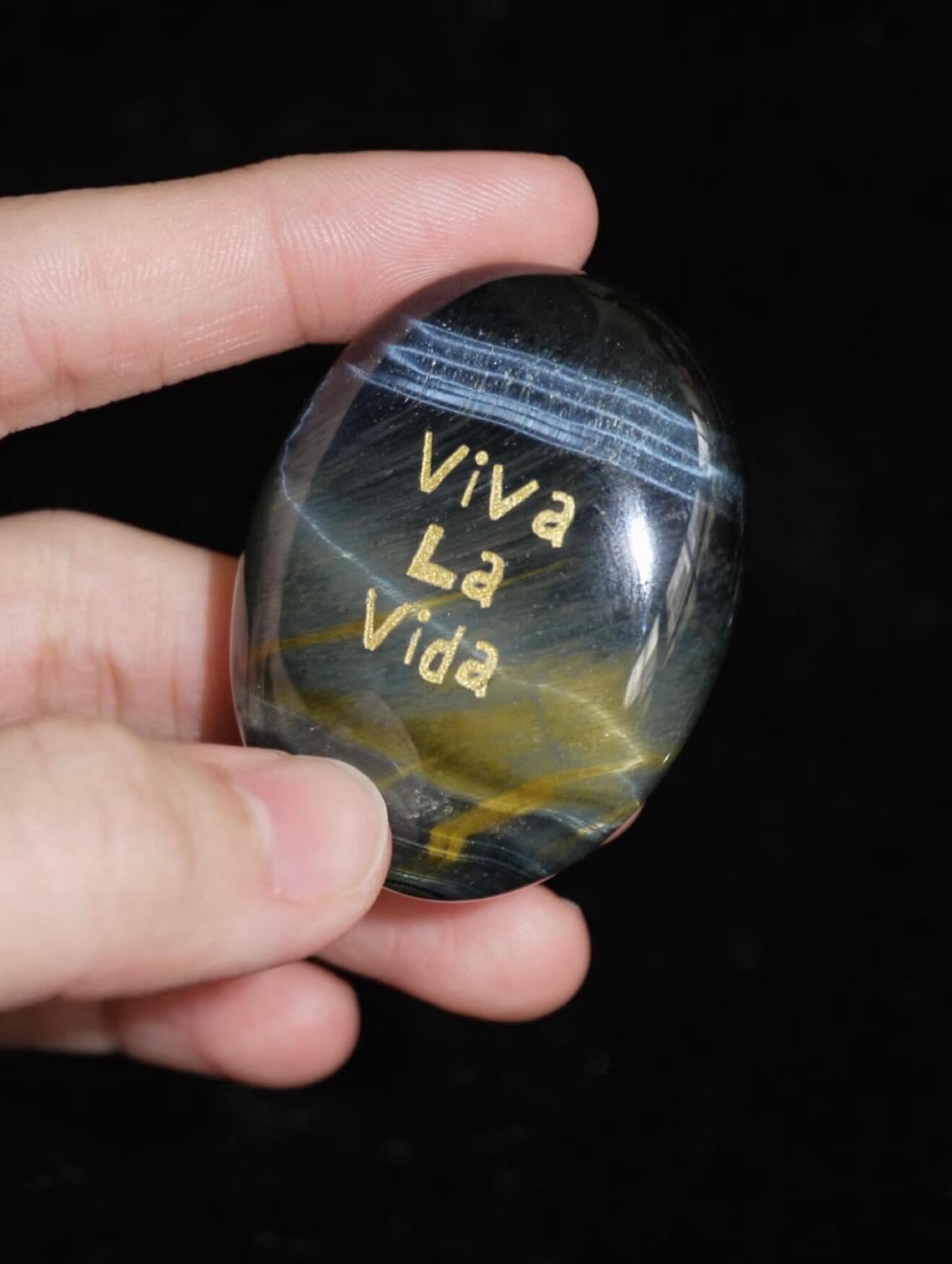 CIRCLEARA "Viva La Vida" etched Blue Tiger's Eye mineral. A tactile grounding tool for calm vitality and gratitude, showcasing natural hawk's eye chatoyancy and gold-leaf lettering.
