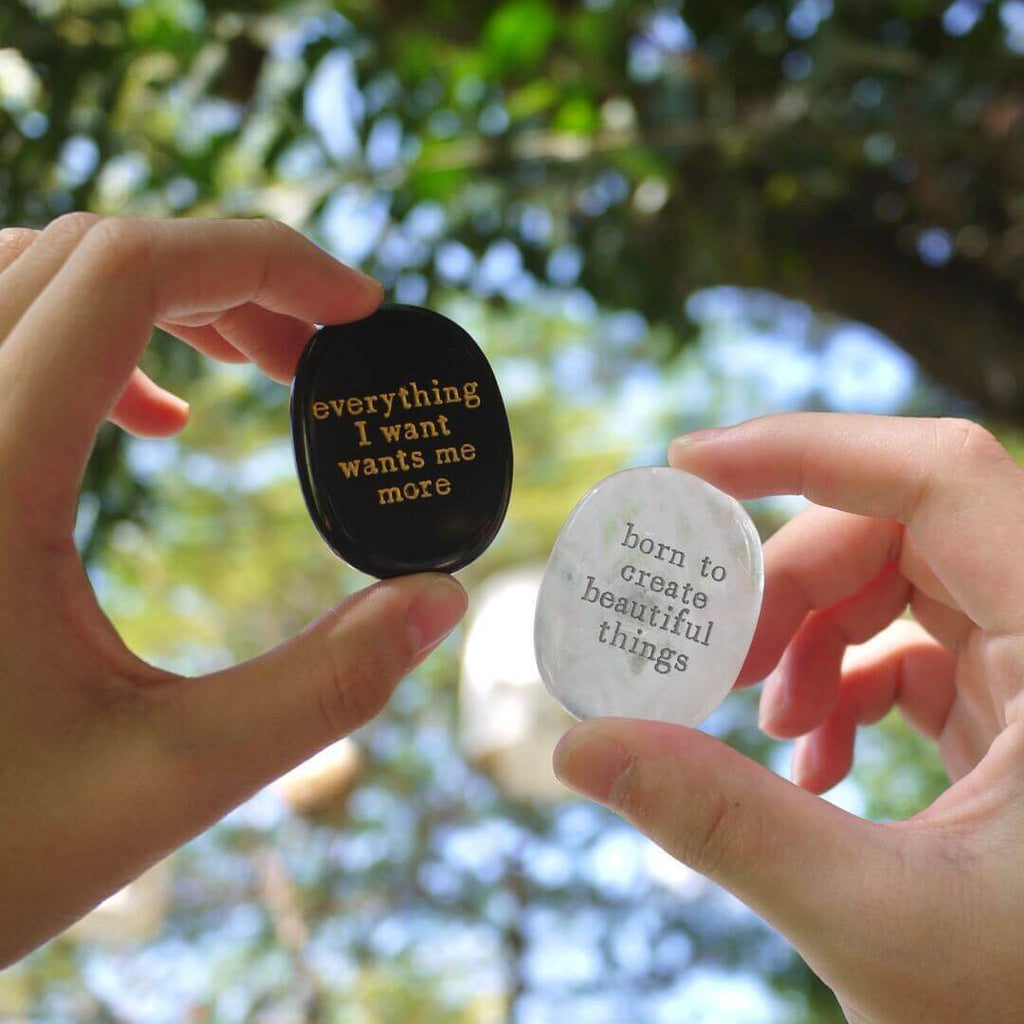 Hand holding a CIRCLEARA etched affirmation crystal stone, translucent texture, "born to create beautiful things" creative manifestation tool.