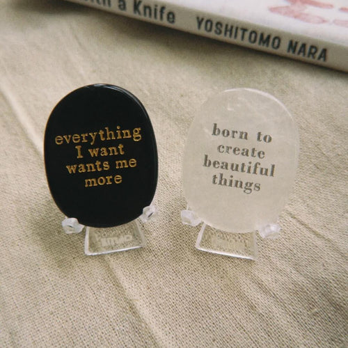 Hand holding a CIRCLEARA etched affirmation crystal stone, translucent texture, "born to create beautiful things" creative manifestation tool.