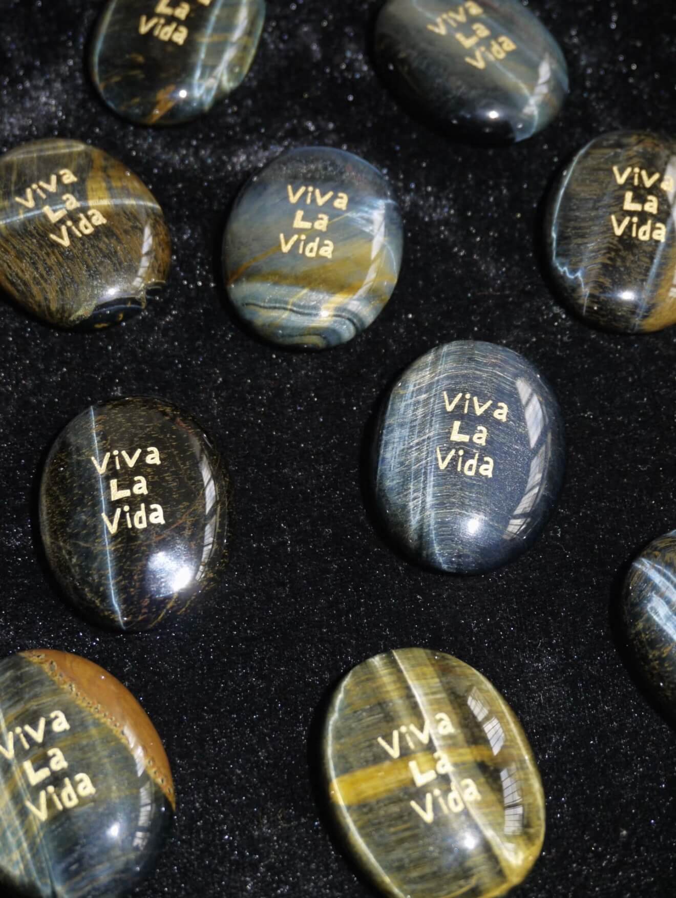 CIRCLEARA "Viva La Vida" etched Blue Tiger's Eye mineral. A tactile grounding tool for calm vitality and gratitude, showcasing natural hawk's eye chatoyancy and gold-leaf lettering.