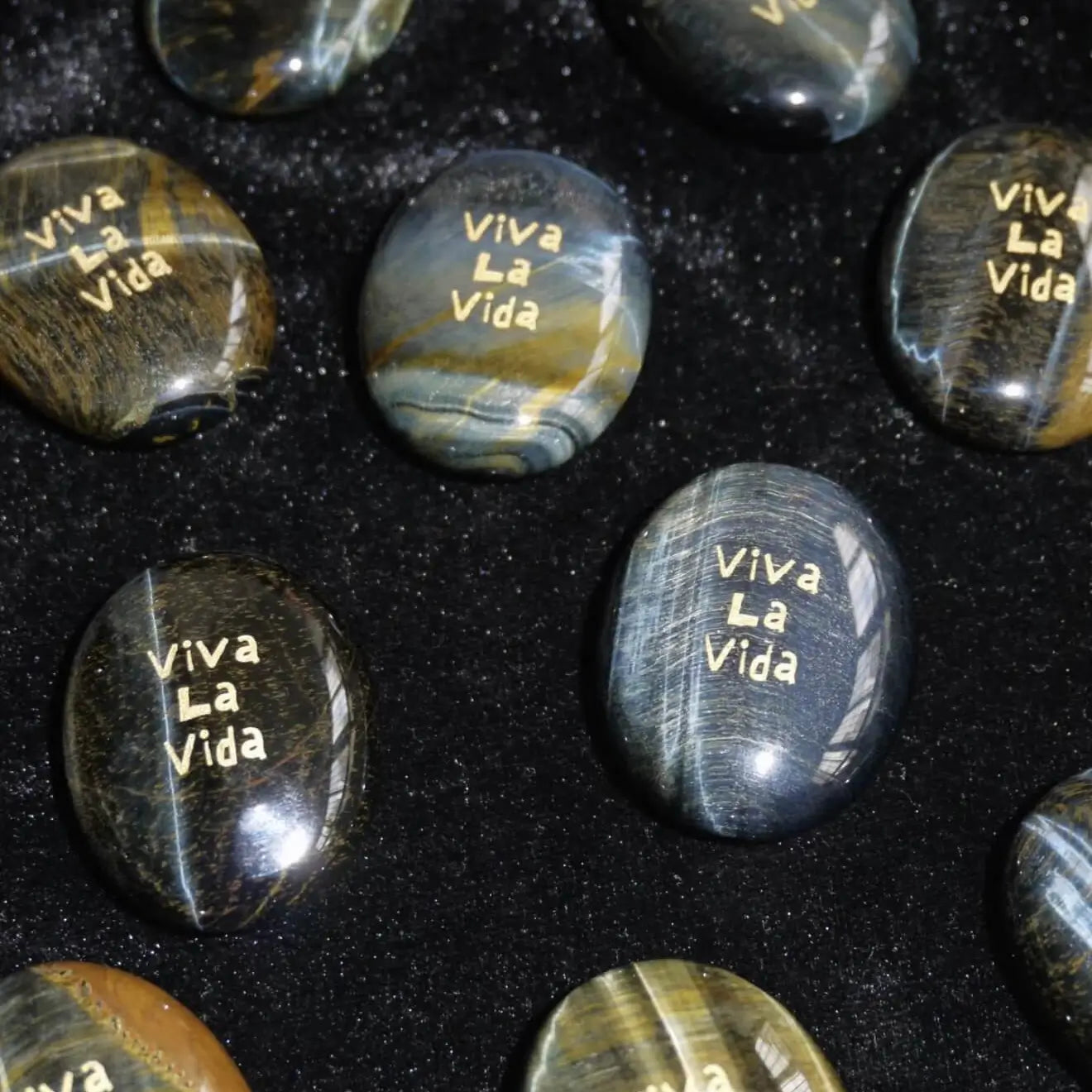 CIRCLEARA "Viva La Vida" etched Blue Tiger's Eye mineral. A tactile grounding tool for calm vitality and gratitude, showcasing natural hawk's eye chatoyancy and gold-leaf lettering.