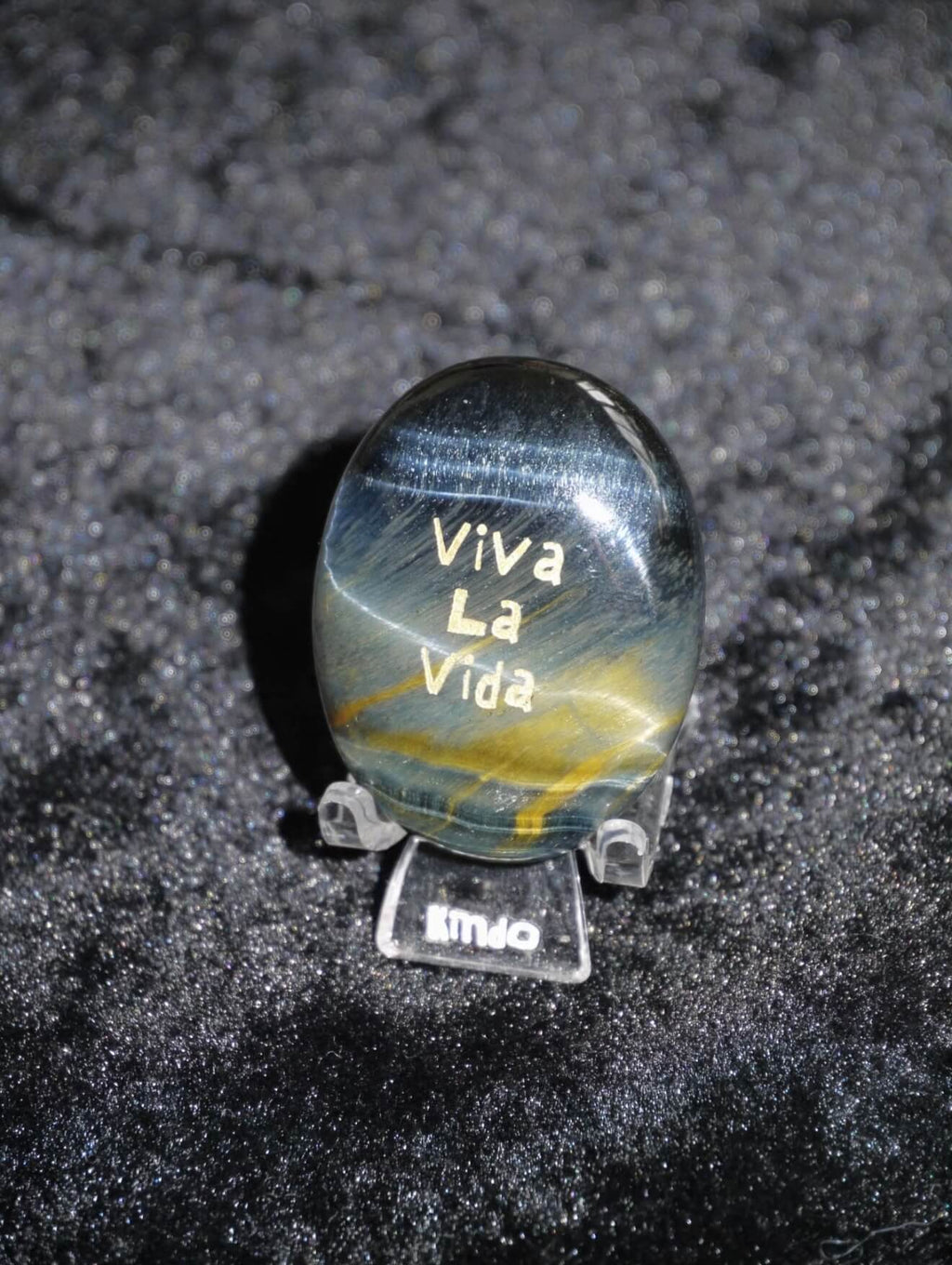 CIRCLEARA "Viva La Vida" etched Blue Tiger's Eye mineral. A tactile grounding tool for calm vitality and gratitude, showcasing natural hawk's eye chatoyancy and gold-leaf lettering.
