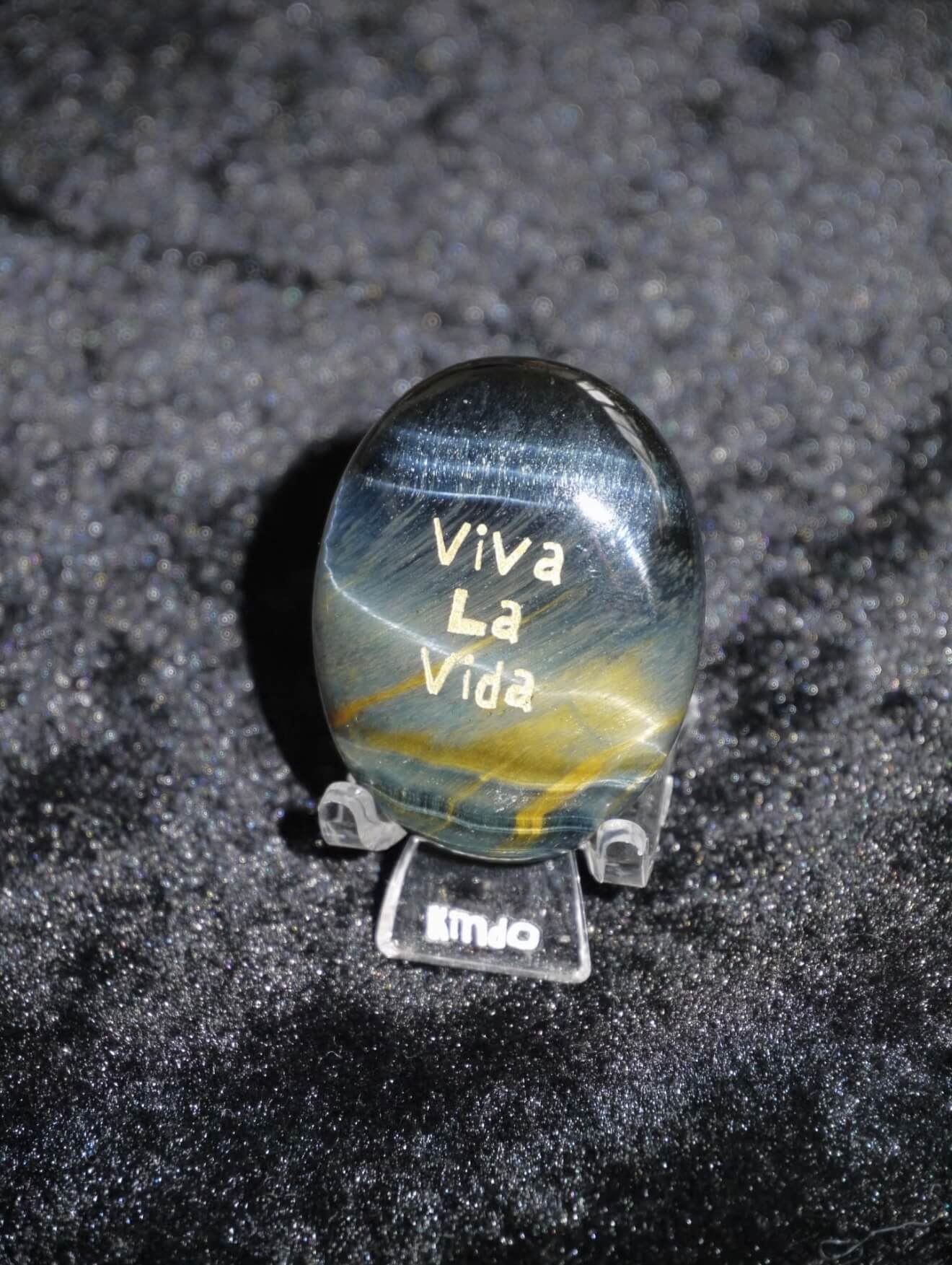 CIRCLEARA "Viva La Vida" etched Blue Tiger's Eye mineral. A tactile grounding tool for calm vitality and gratitude, showcasing natural hawk's eye chatoyancy and gold-leaf lettering.