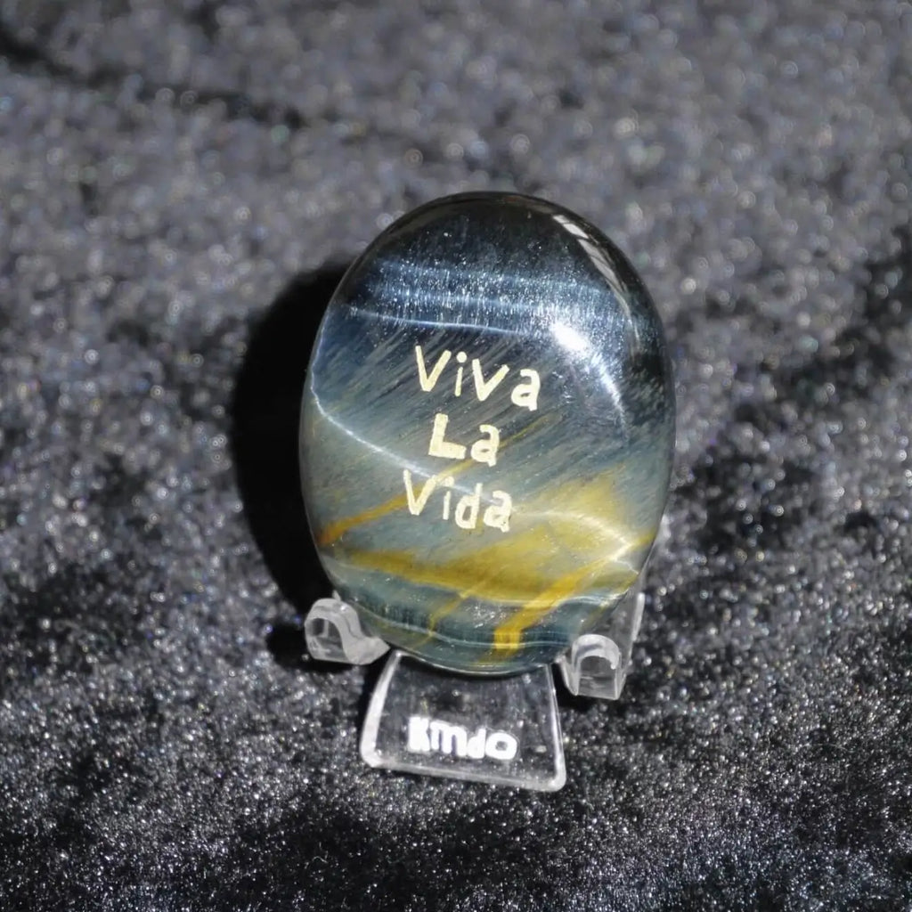 CIRCLEARA "Viva La Vida" etched Blue Tiger's Eye mineral. A tactile grounding tool for calm vitality and gratitude, showcasing natural hawk's eye chatoyancy and gold-leaf lettering.