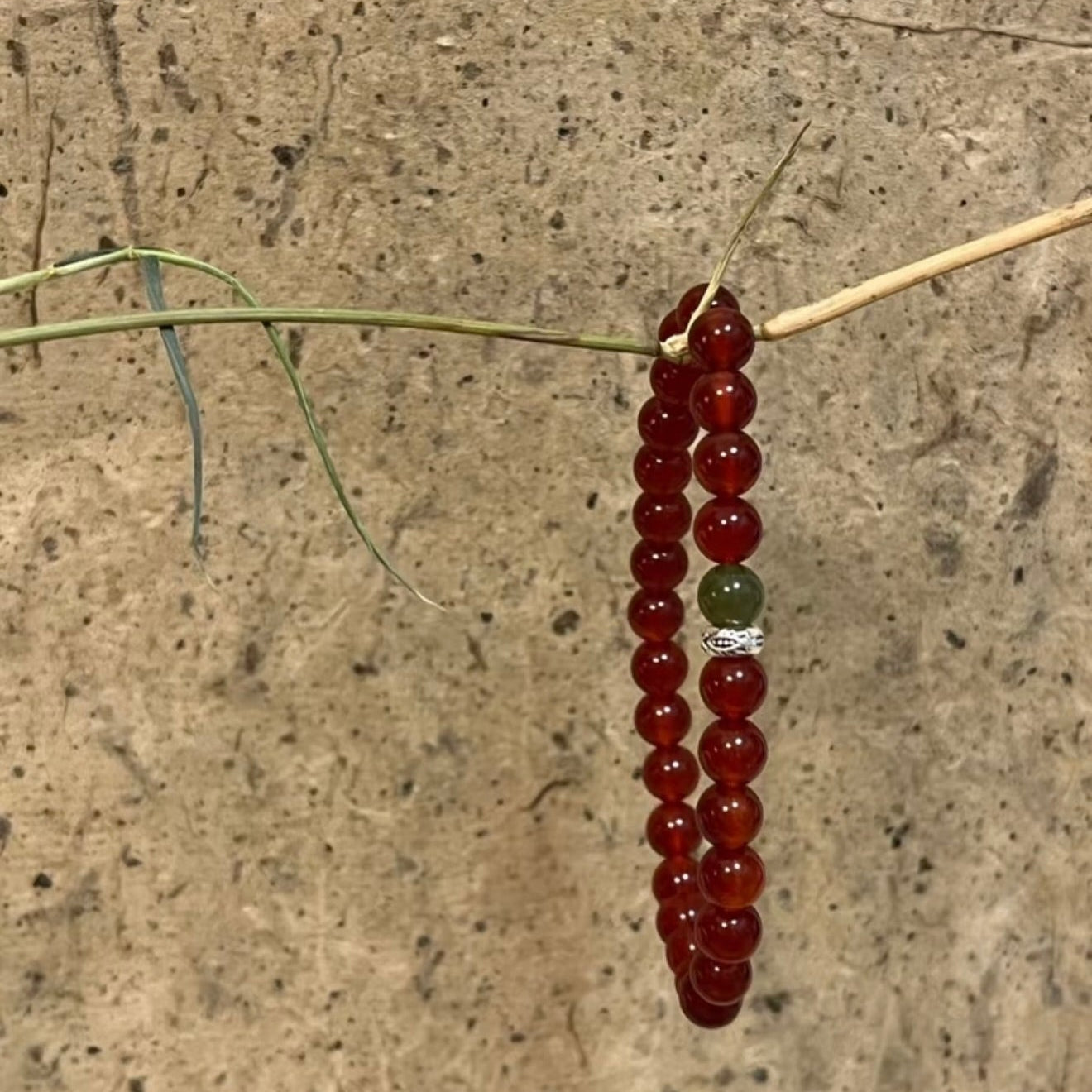 A handcrafted CIRCLEARA He Huan bracelet with 6mm red agate and a single green jade bead, styled in a minimalist earthen setting.