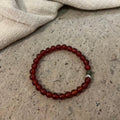 A handcrafted CIRCLEARA He Huan bracelet with 6mm red agate and a single green jade bead, styled in a minimalist earthen setting.
