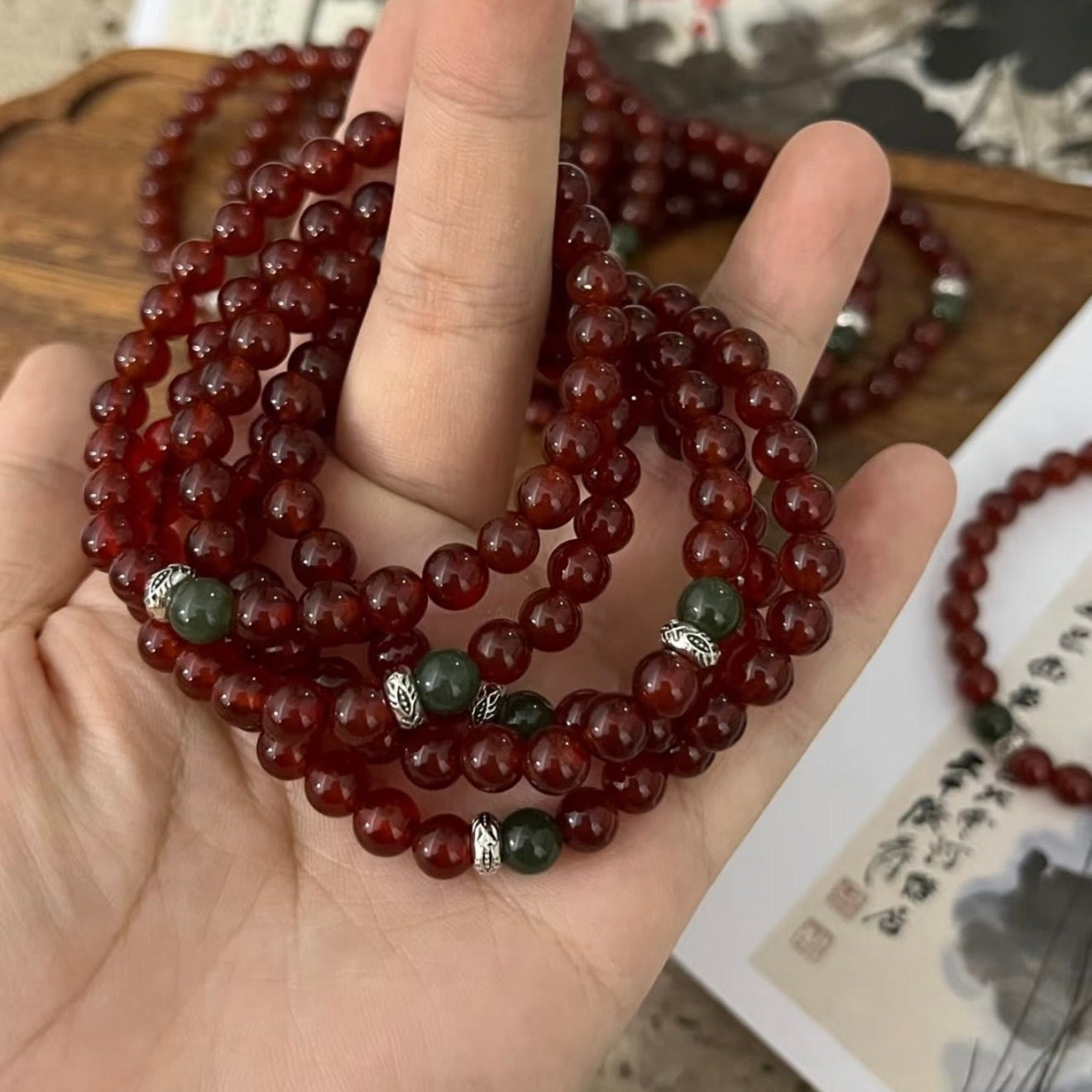 A handcrafted CIRCLEARA He Huan bracelet with 6mm red agate and a single green jade bead, styled in a minimalist earthen setting.