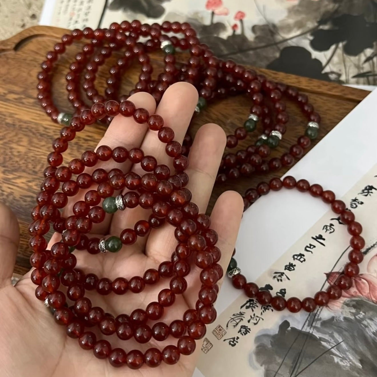 A handcrafted CIRCLEARA He Huan bracelet with 6mm red agate and a single green jade bead, styled in a minimalist earthen setting.