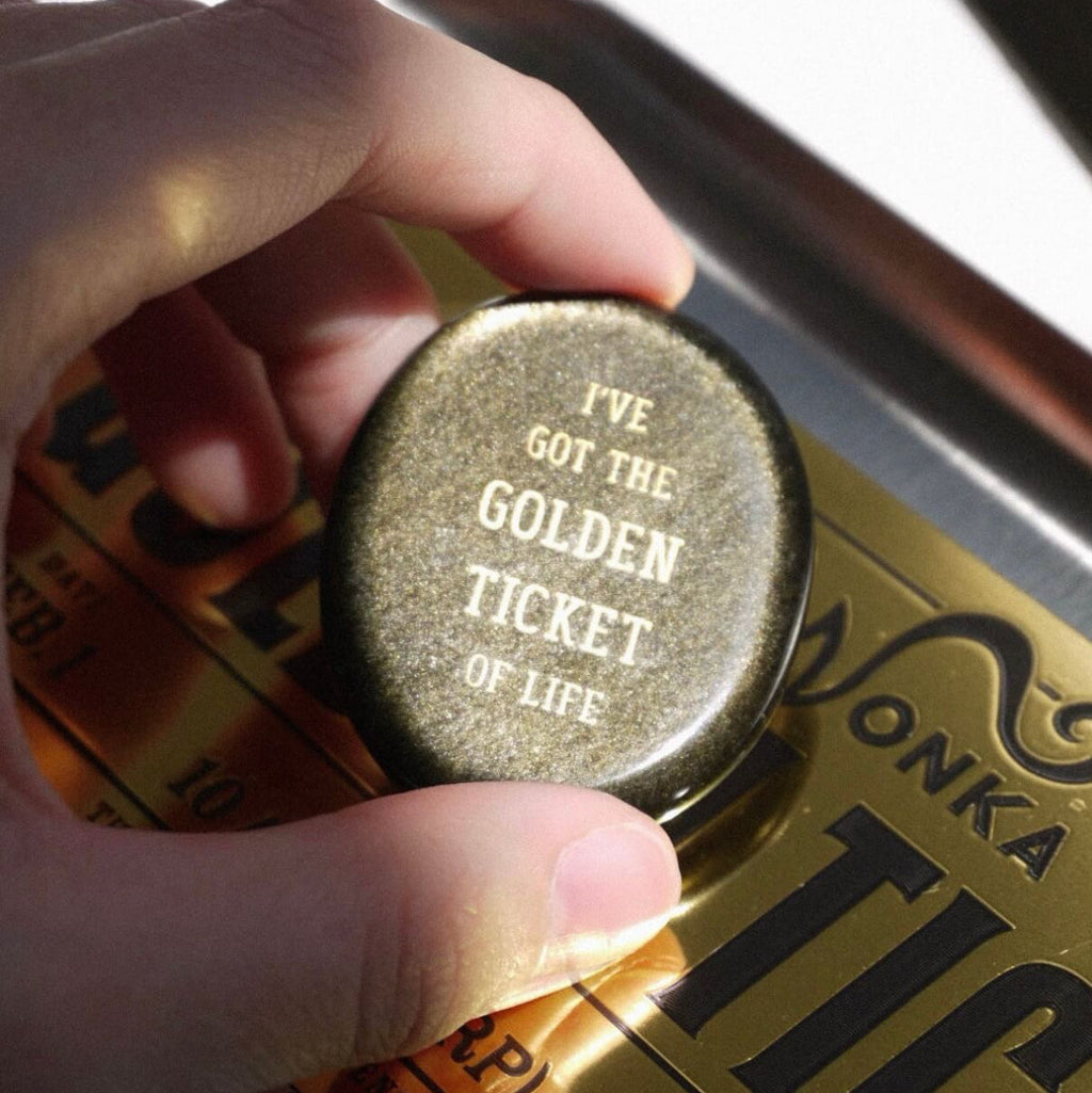 CIRCLEARA "Golden Ticket" manifest stone. Deep sheen mineral with gold-etched motivational mantra, designed as a tactile artifact for owning your abundance.
