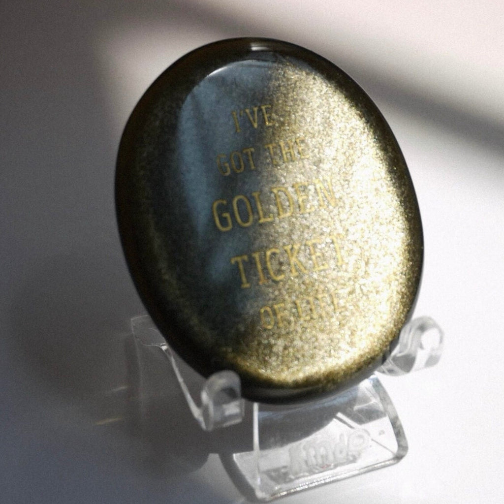 CIRCLEARA "Golden Ticket" manifest stone. Deep sheen mineral with gold-etched motivational mantra, designed as a tactile artifact for owning your abundance.