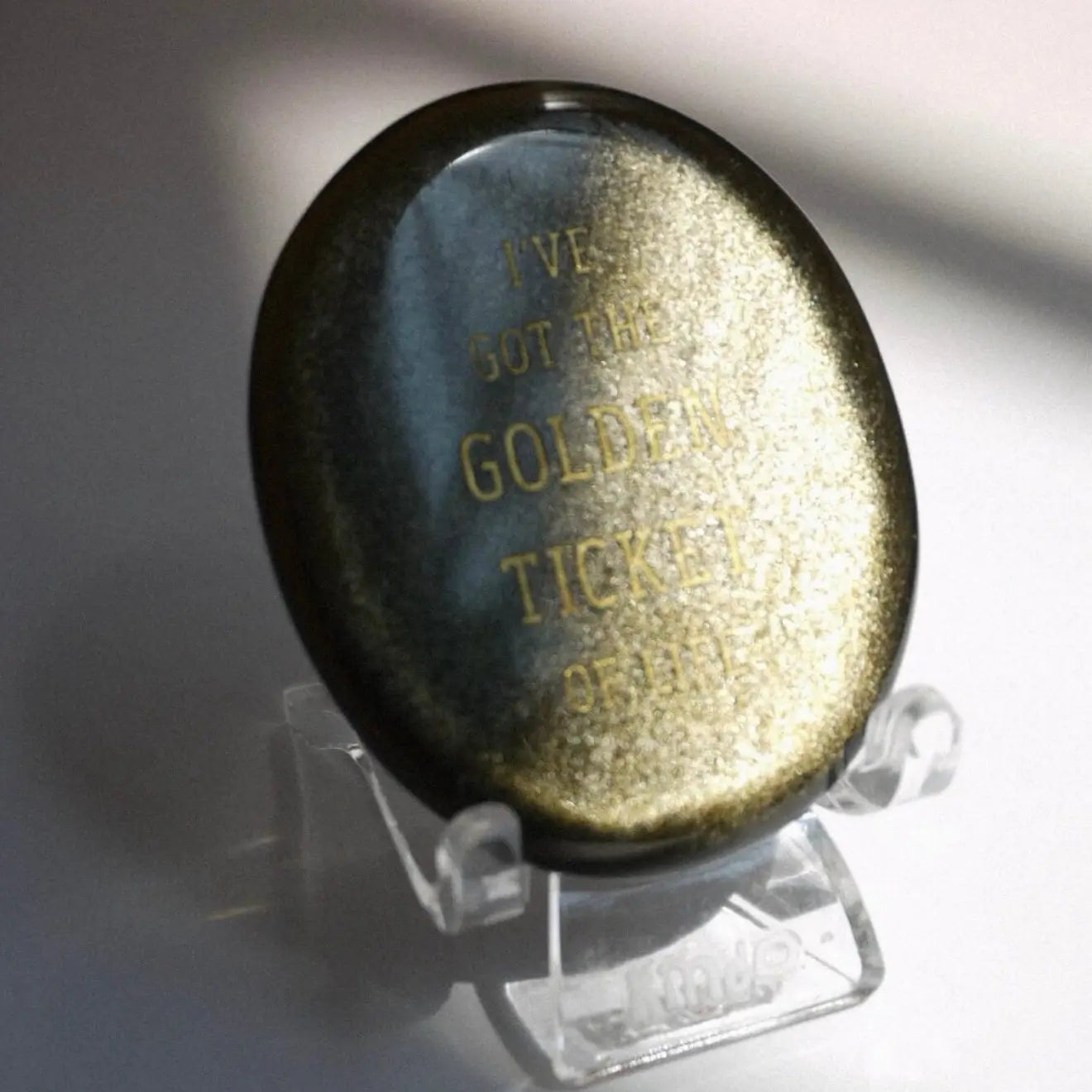 CIRCLEARA "Golden Ticket" manifest stone. Deep sheen mineral with gold-etched motivational mantra, designed as a tactile artifact for owning your abundance.