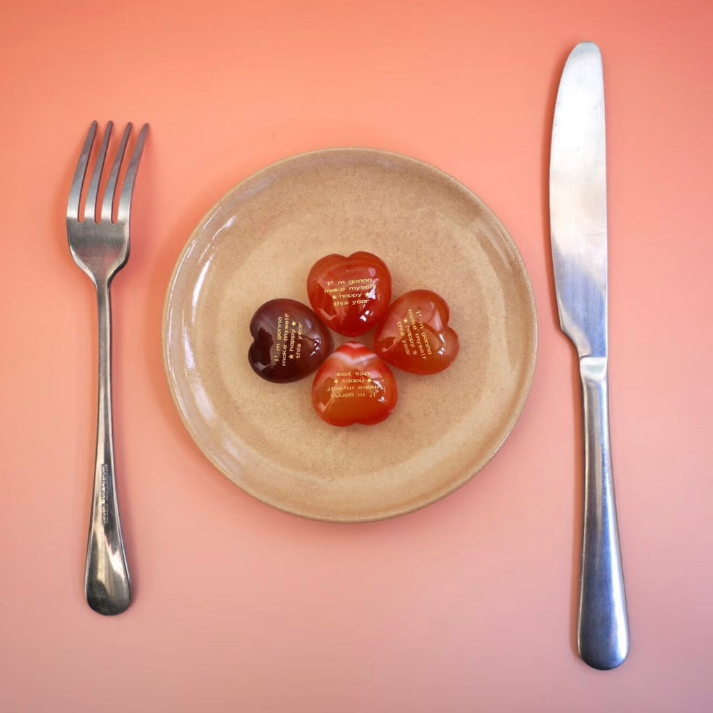CIRCLEARA "Self-Happy" etched Carnelian heart. A tactile grounding mineral for emotional warmth and vitality, presented as a symbolic 'mental meal' on a dinner plate to represent self-care.