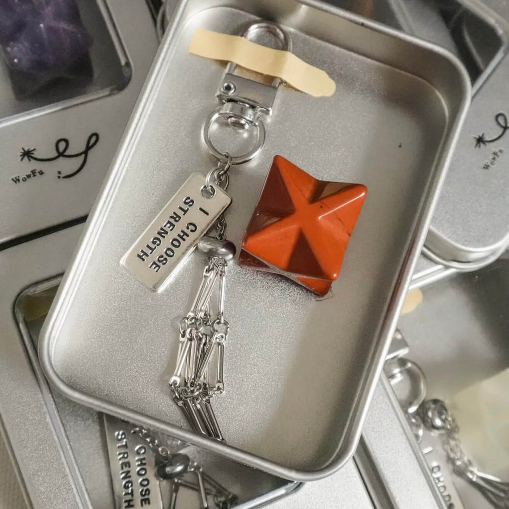 Handcrafted Red Jasper Merkaba star sacred geometry crystal accessory, featuring a protective alloy cage, heavy-duty keyring clip, and motivational tag on a minimalist background.