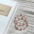 Two handcrafted Rose Quartz and Southern Red Agate grounding bracelets with white shell accents, displayed on a textured linen cloth alongside an artistic vintage book.