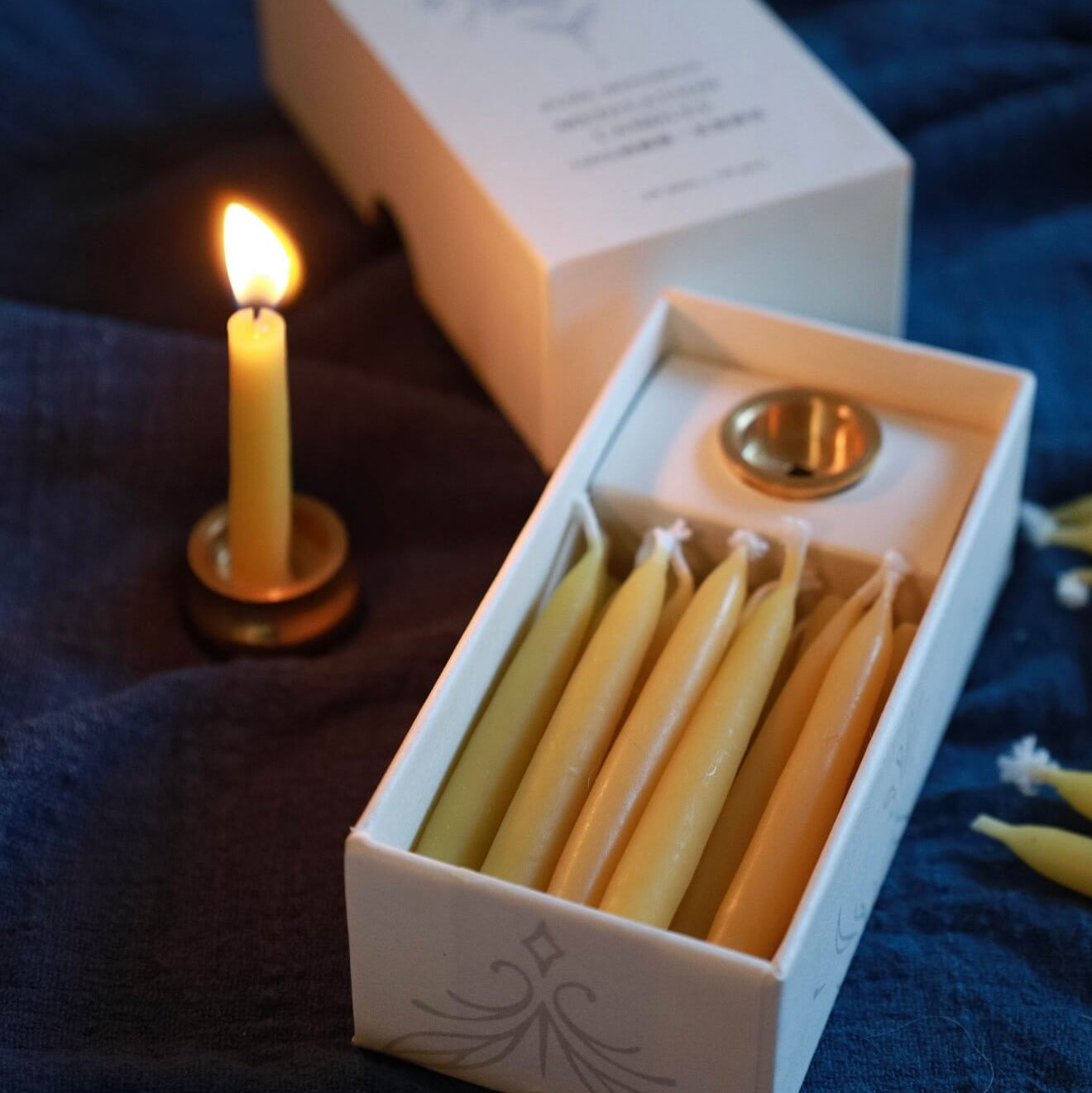 A single slim beeswax candle burning in a brass holder with a warm, steady flame, emphasizing a 20-minute peaceful meditation session.