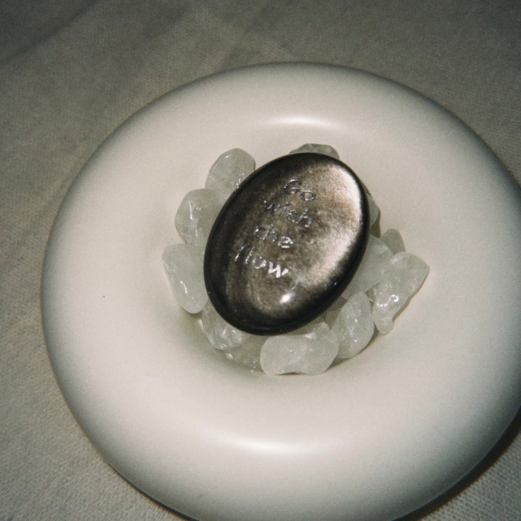Handcrafted natural dark mystic stone with silver-etched inscription 'Go with the flow' by CIRCLEARA, resting on a minimalist white ceramic display holder.