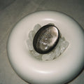Handcrafted natural dark mystic stone with silver-etched inscription 'Go with the flow' by CIRCLEARA, resting on a minimalist white ceramic display holder.