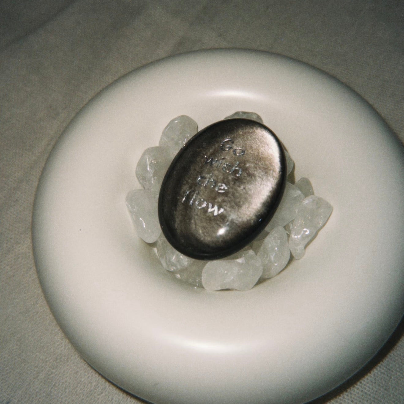 Handcrafted natural dark mystic stone with silver-etched inscription 'Go with the flow' by CIRCLEARA, resting on a minimalist white ceramic display holder.