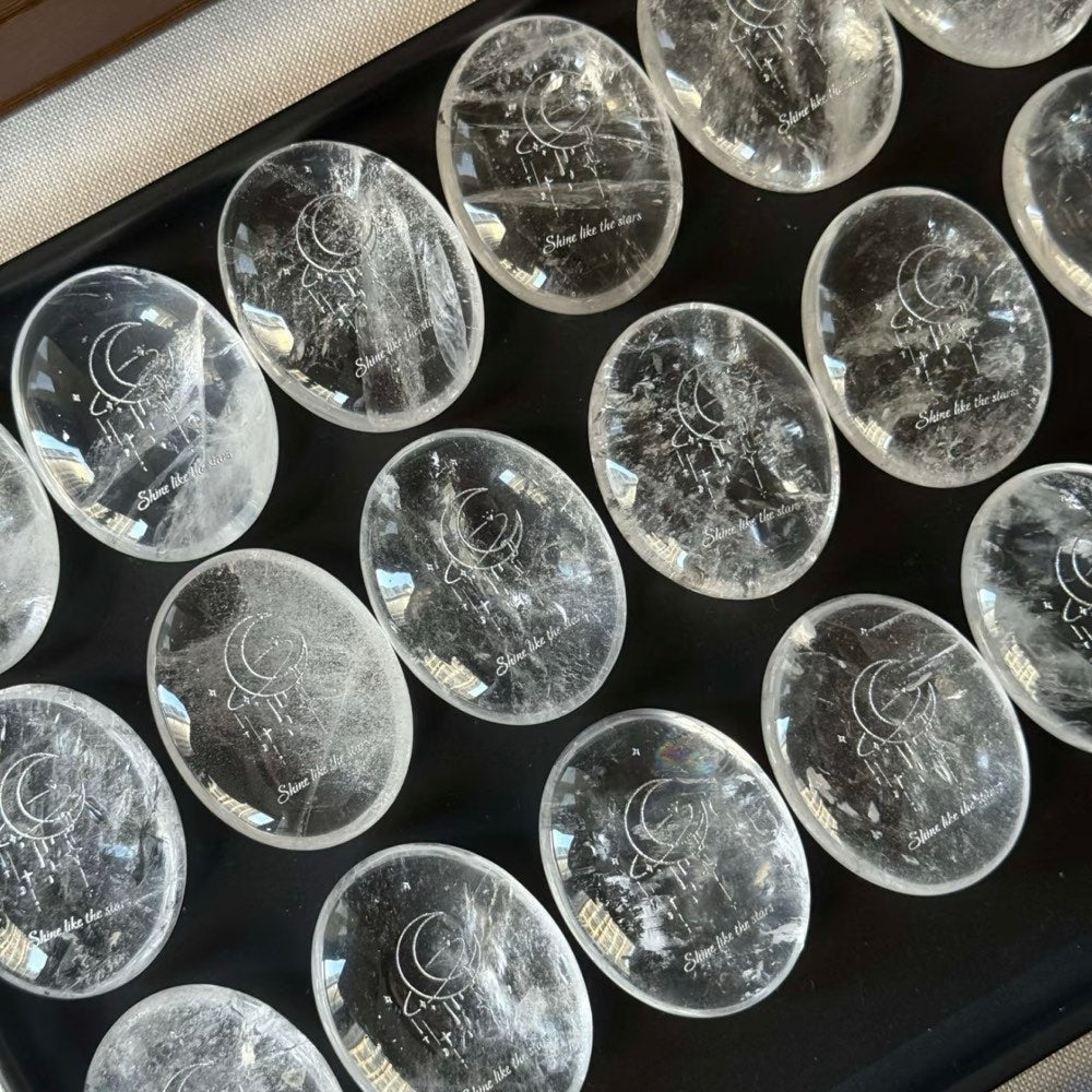 Handcrafted 45mm natural Clear Quartz cosmic palm stones by CIRCLEARA, silver-etched with a crescent moon and starbursts, showing organic internal ice-crack textures.