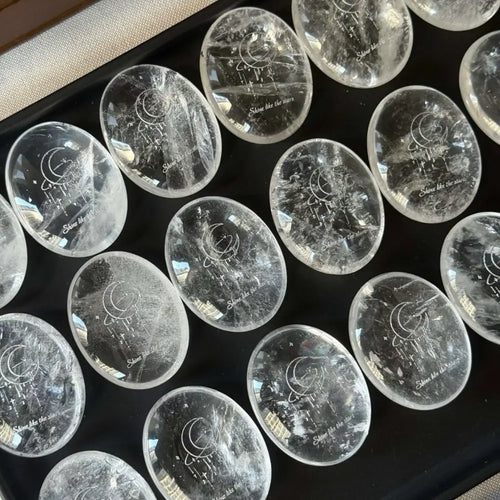 Handcrafted 45mm natural Clear Quartz cosmic palm stones by CIRCLEARA, silver-etched with a crescent moon and starbursts, showing organic internal ice-crack textures.
