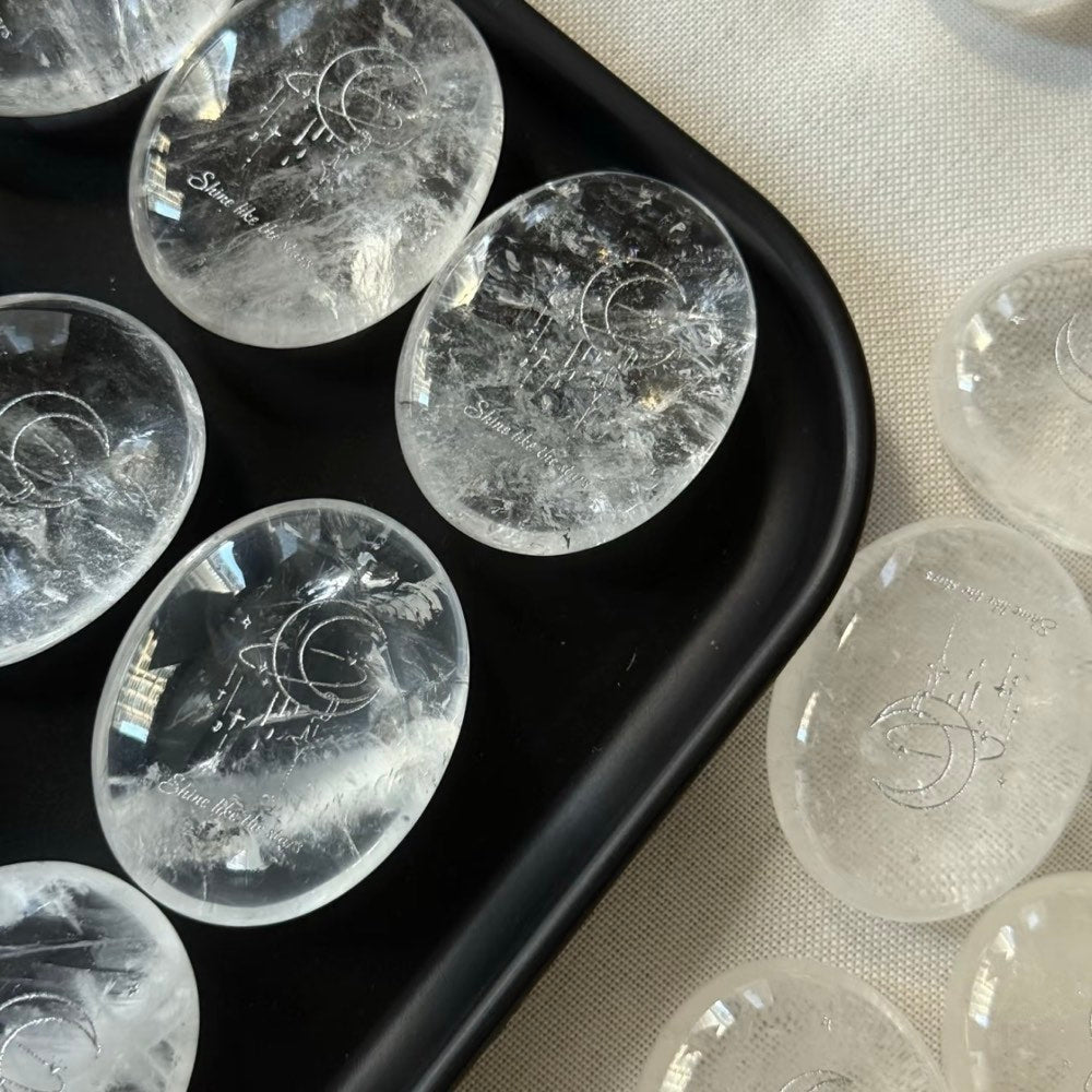 Handcrafted 45mm natural Clear Quartz cosmic palm stones by CIRCLEARA, silver-etched with a crescent moon and starbursts, showing organic internal ice-crack textures.