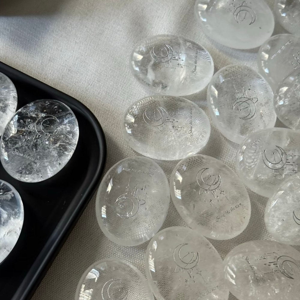 Handcrafted 45mm natural Clear Quartz cosmic palm stones by CIRCLEARA, silver-etched with a crescent moon and starbursts, showing organic internal ice-crack textures.