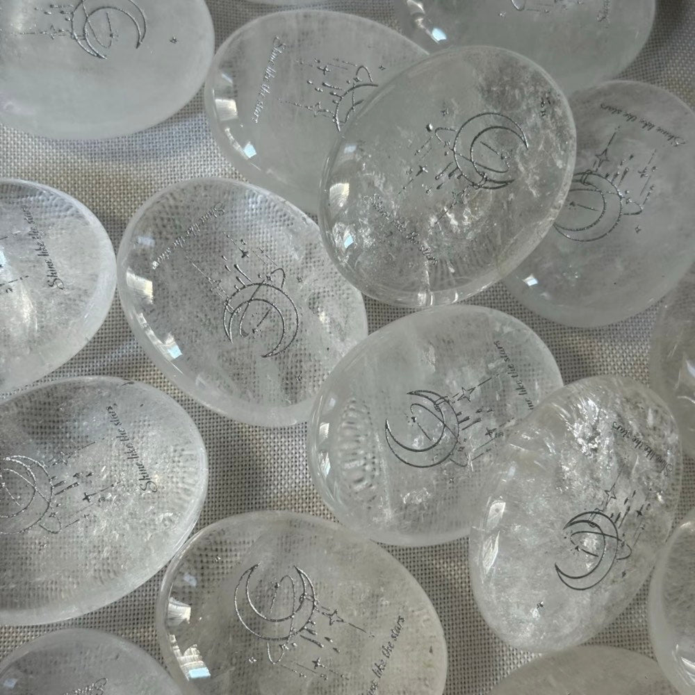 Handcrafted 45mm natural Clear Quartz cosmic palm stones by CIRCLEARA, silver-etched with a crescent moon and starbursts, showing organic internal ice-crack textures.