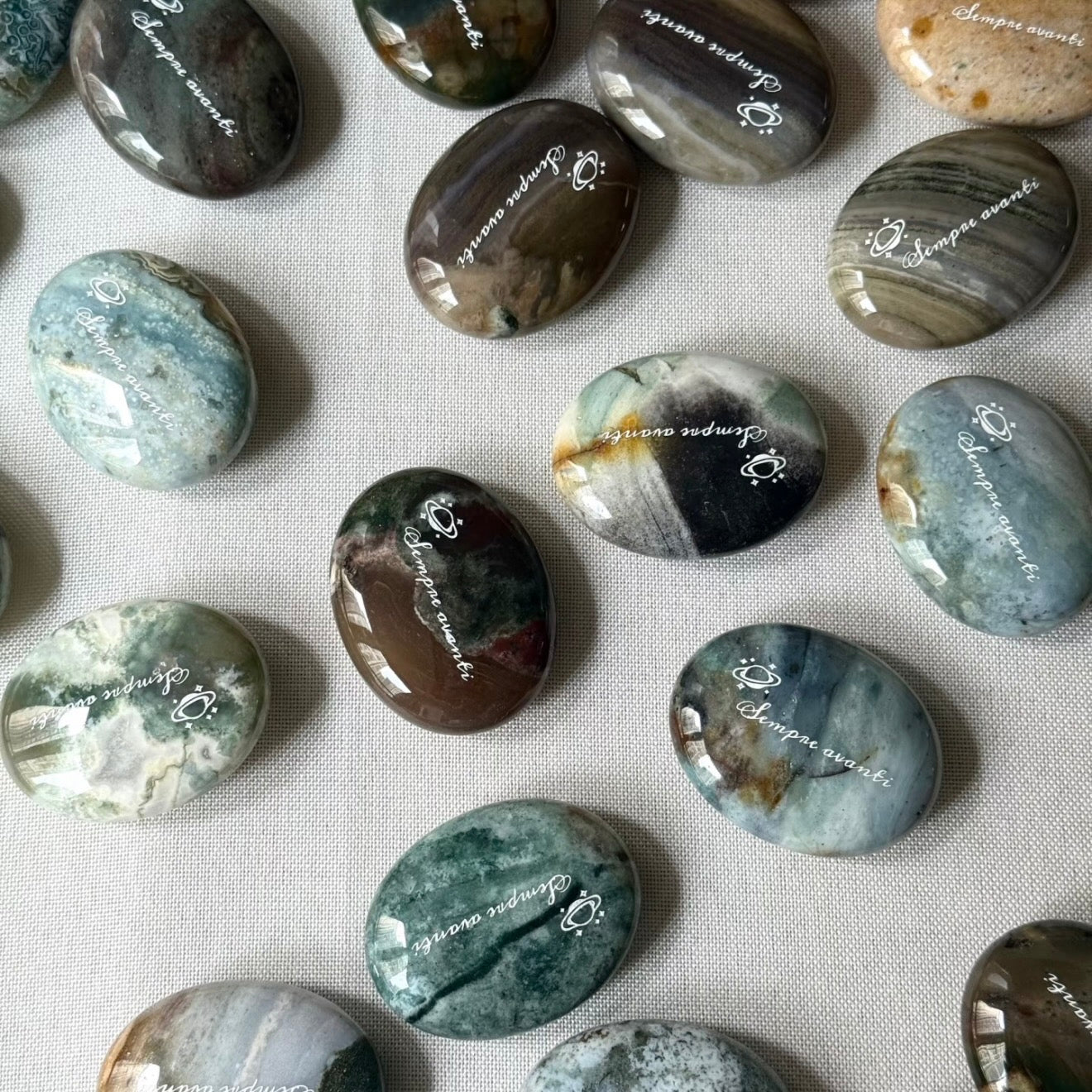 Handcrafted 45mm natural Ocean Jasper cosmic palm stones by CIRCLEARA, engraved with silver text 'KEEP MOVING' and a starburst symbol, displaying unique green and white orbicular textures.