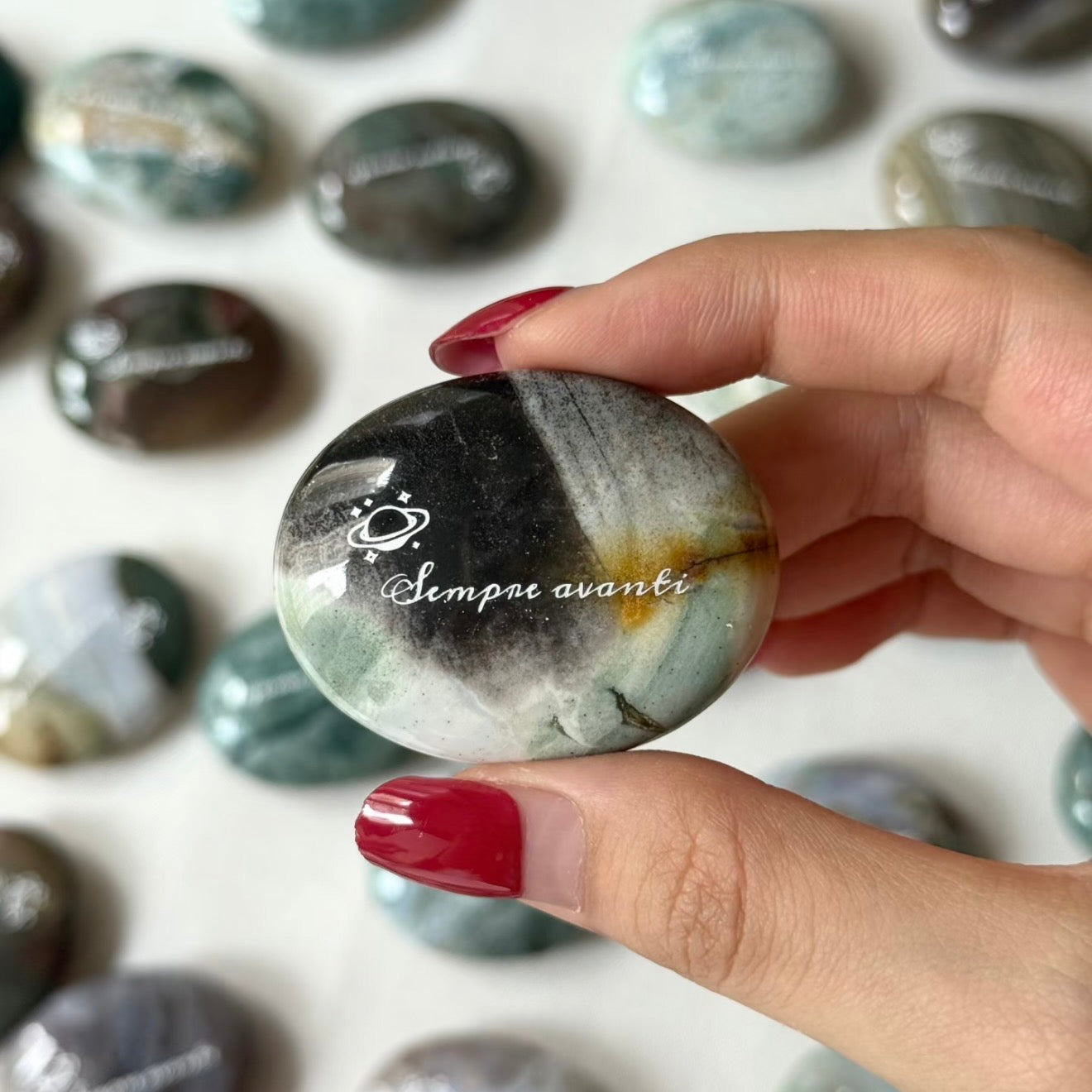 Handcrafted 45mm natural Ocean Jasper cosmic palm stones by CIRCLEARA, engraved with silver text 'KEEP MOVING' and a starburst symbol, displaying unique green and white orbicular textures.