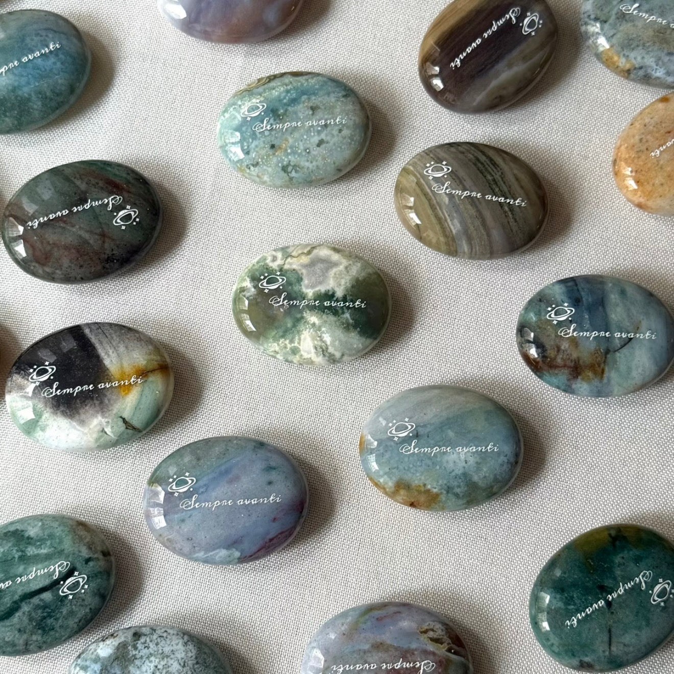 Handcrafted 45mm natural Ocean Jasper cosmic palm stones by CIRCLEARA, engraved with silver text 'KEEP MOVING' and a starburst symbol, displaying unique green and white orbicular textures.