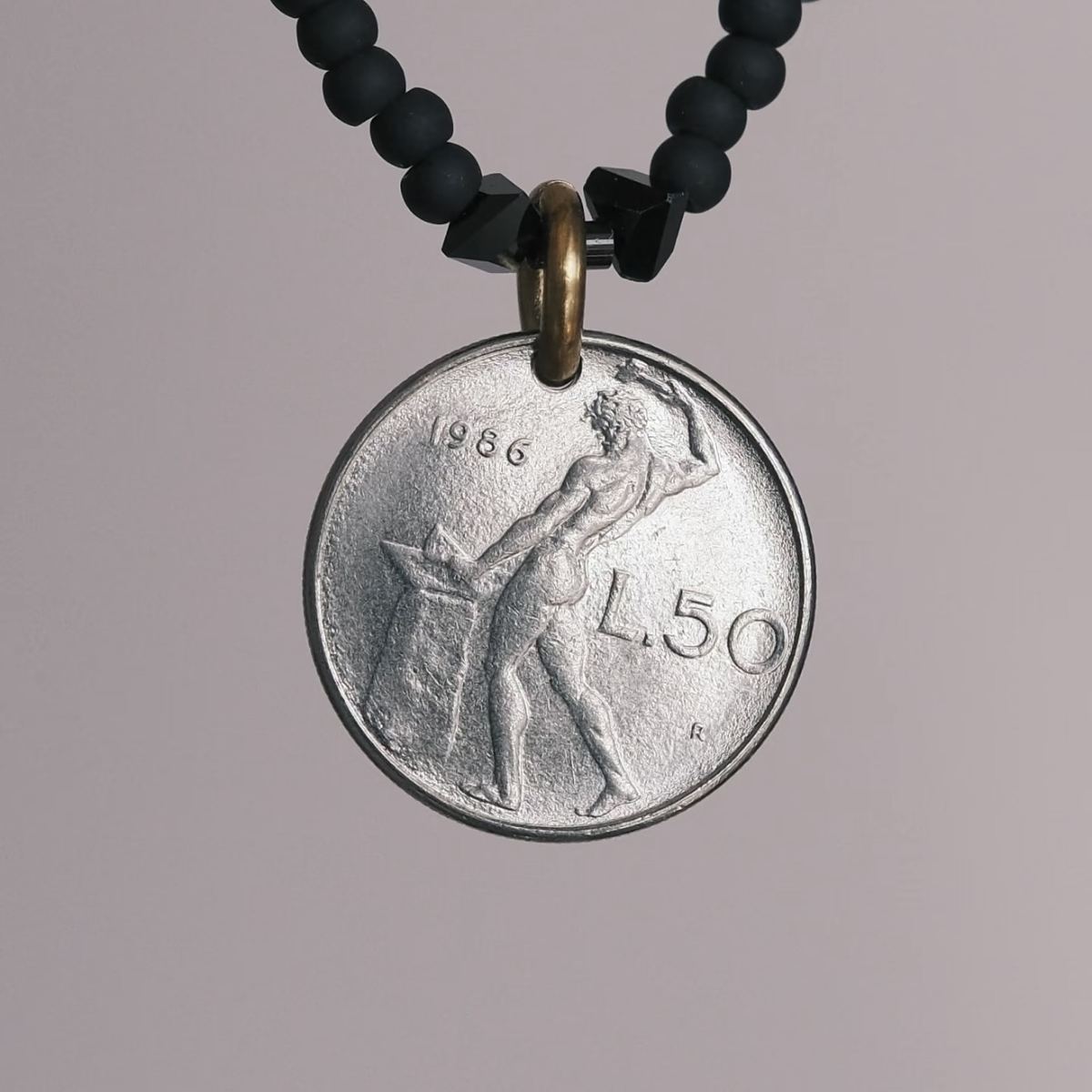 Close-up shot of CIRCLEARA boundary necklace featuring a weighted silver vintage coin pendant with an engraved classical deity, connected by a brass bail to premium Japanese Miyuki matte black glass beads.