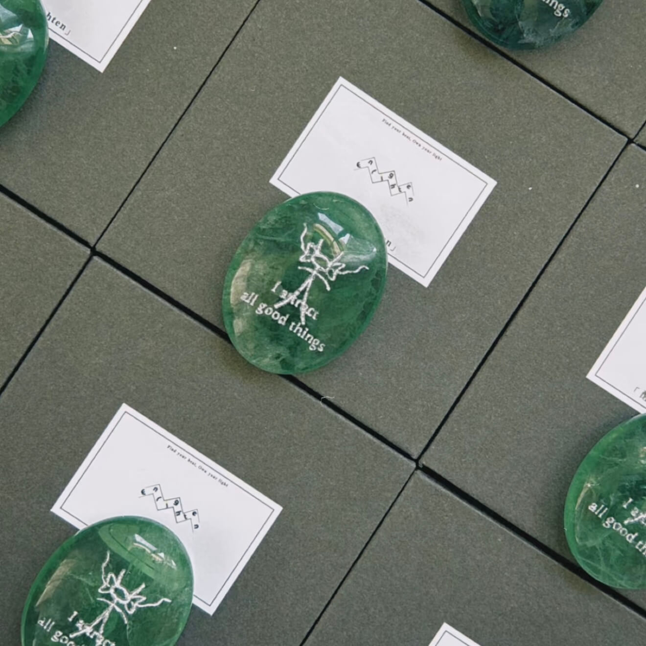 A front-facing detailed shot of the translucent green fluorite CIRCLEARA palm stone resting on its complimentary clear minimalist stand, revealing the precise Dongba pictograph and the etched phrase "I attract all good things."