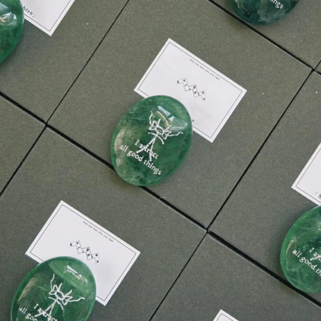 A front-facing detailed shot of the translucent green fluorite CIRCLEARA palm stone resting on its complimentary clear minimalist stand, revealing the precise Dongba pictograph and the etched phrase "I attract all good things."