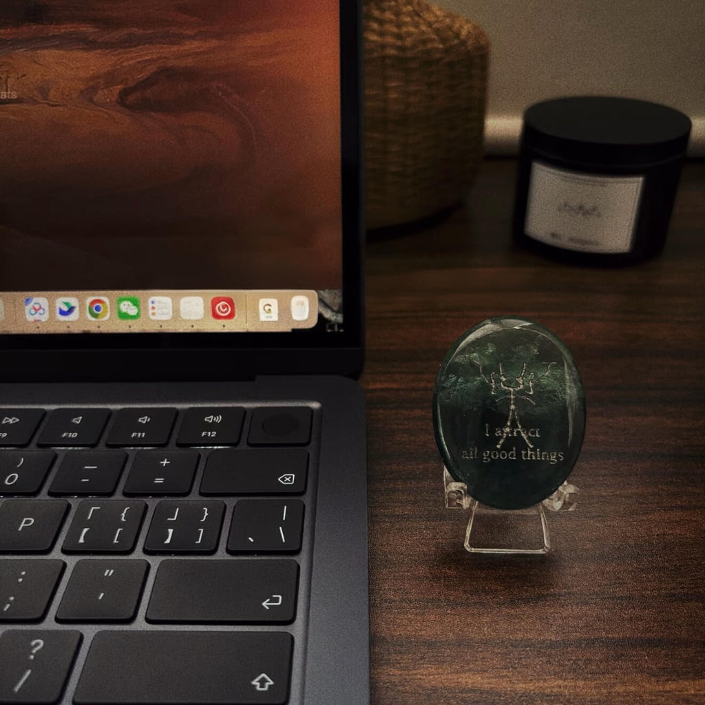 A front-facing detailed shot of the translucent green fluorite CIRCLEARA palm stone resting on its complimentary clear minimalist stand, revealing the precise Dongba pictograph and the etched phrase "I attract all good things."