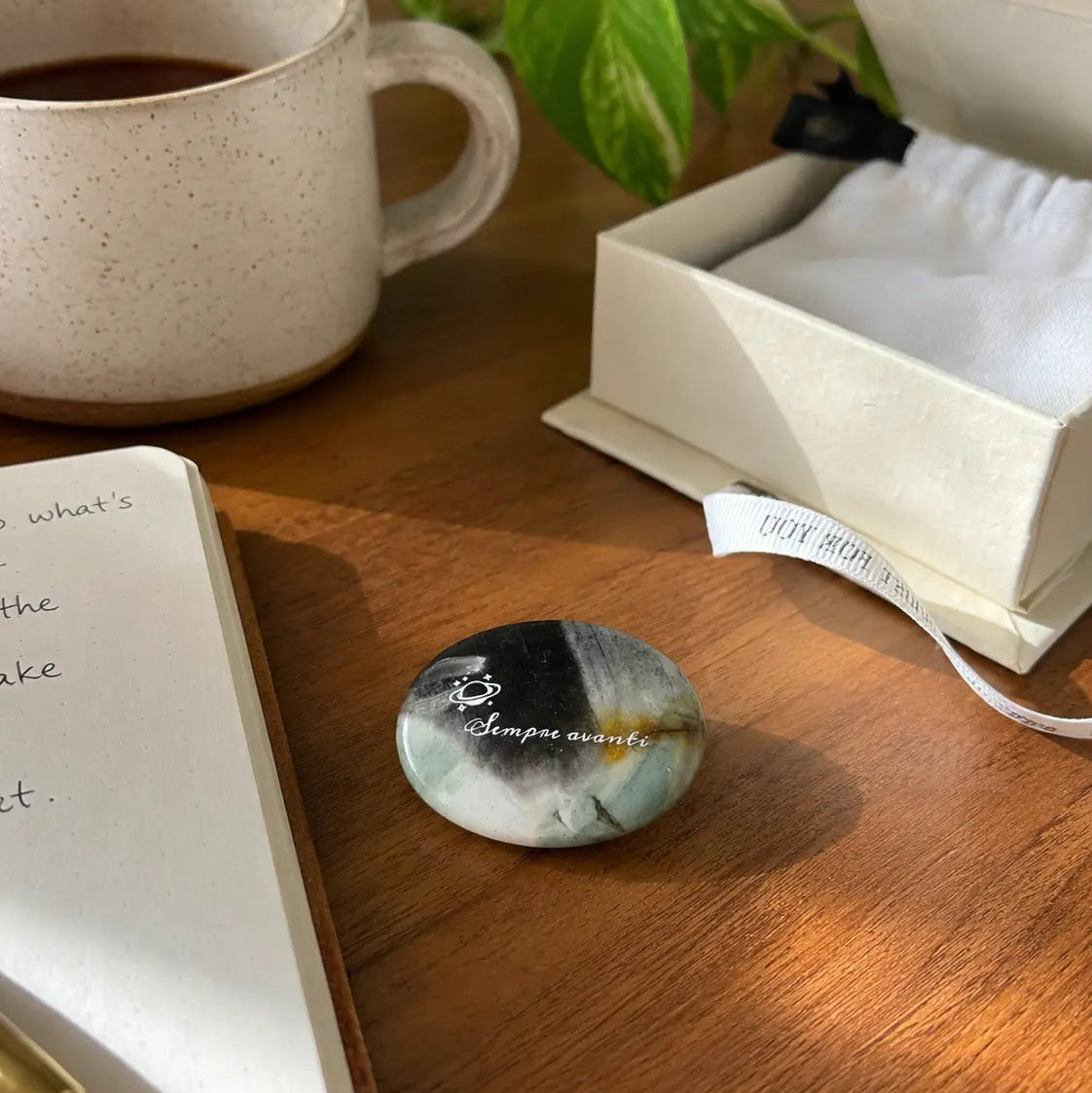Natural polished labradorite affirmation stone with engraved “Sempre avanti” message, held in hand with crystal stones in the background.