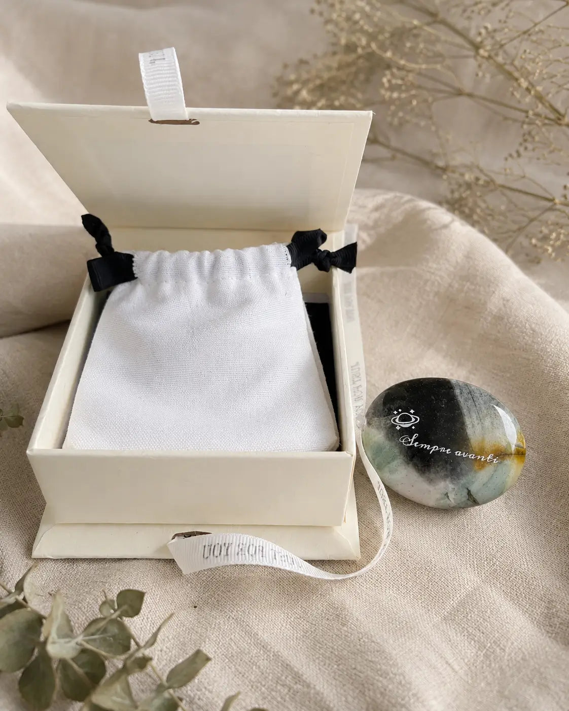Natural polished labradorite affirmation stone with engraved “Sempre avanti” message, held in hand with crystal stones in the background.