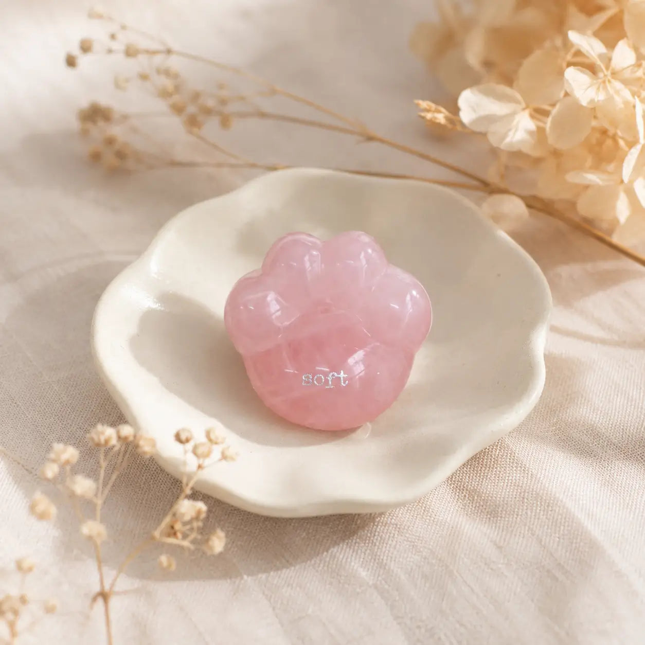 A close-up shot of a hand gently cradling the smooth, translucent pink rose quartz CIRCLEARA palm stone shaped like a rounded cat paw pad with the etched text "soft".