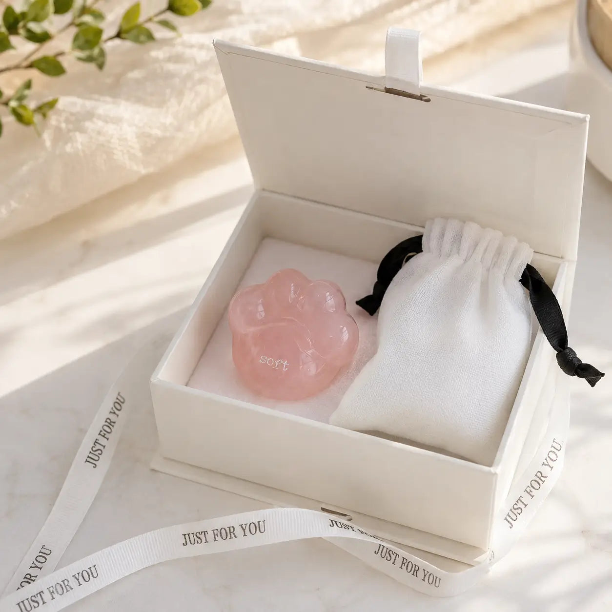 A close-up shot of a hand gently cradling the smooth, translucent pink rose quartz CIRCLEARA palm stone shaped like a rounded cat paw pad with the etched text "soft".