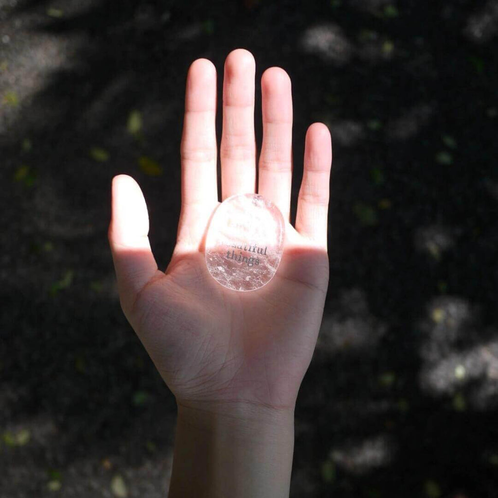 Hand holding a CIRCLEARA etched affirmation crystal stone, translucent texture, "born to create beautiful things" creative manifestation tool.