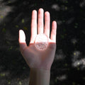 Hand holding a CIRCLEARA etched affirmation crystal stone, translucent texture, "born to create beautiful things" creative manifestation tool.