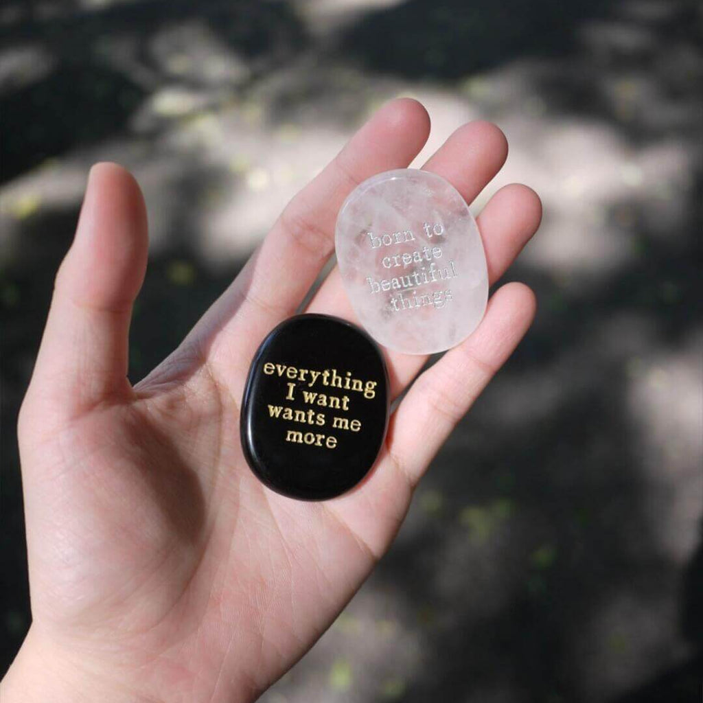 Hand holding a CIRCLEARA etched affirmation crystal stone, translucent texture, "born to create beautiful things" creative manifestation tool.